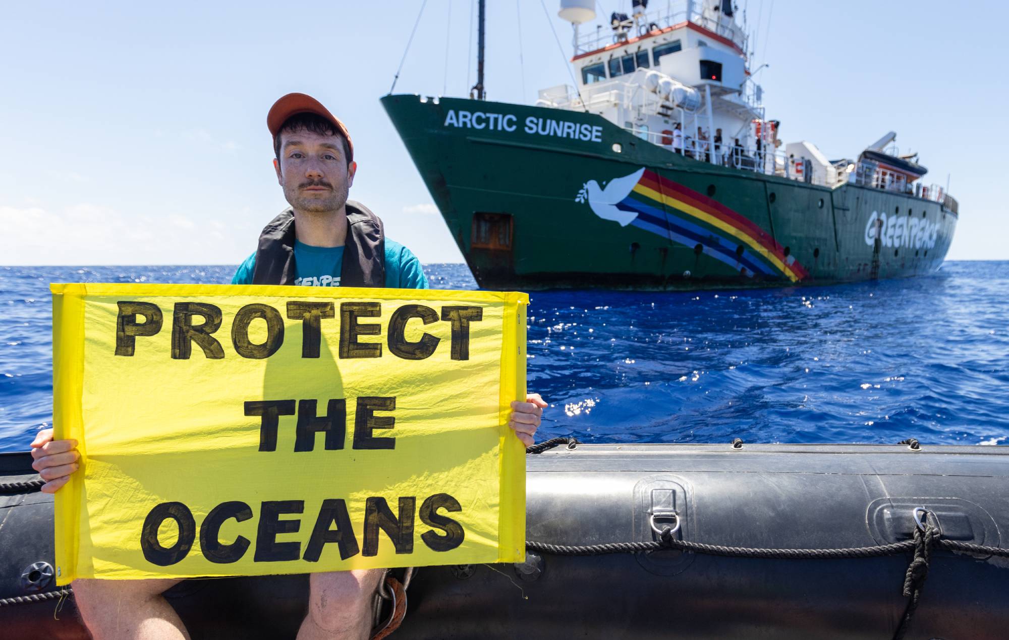 Dan Smith, Bastille on a rhib in front of the Arctic Sunrise with a Protect the Oceans banner. Credit: Press